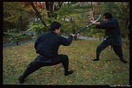 Aka-chan swings the naginata back around and strikes at Kubo-chan's wrist with the blade.